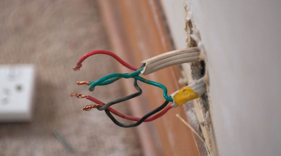 Exposed electrical wires from a wall outlet, with red, green, black, and grey wires, highlighting electrical safety concerns.