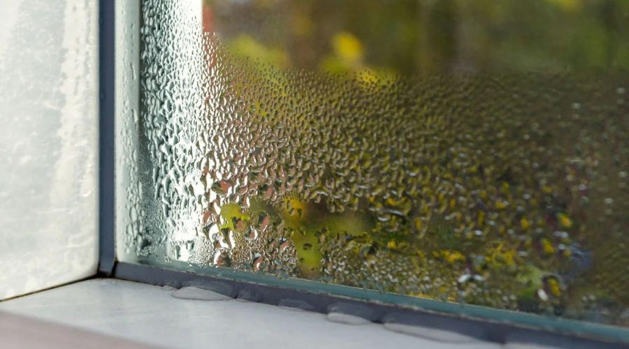 Condensation on a clear window frame with water droplets, highlighting seasonal home maintenance for The Bosworth Company.