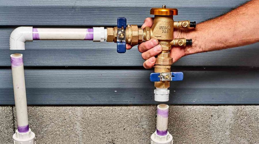 Hand holding a brass valve connected to white PVC pipes, showcasing a plumbing solution by The Bosworth Company.