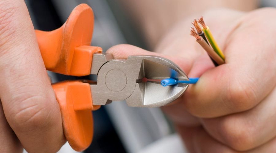 Hands using pliers to cut electrical wires, showcasing DIY skills for The Bosworth Company's electrical services.