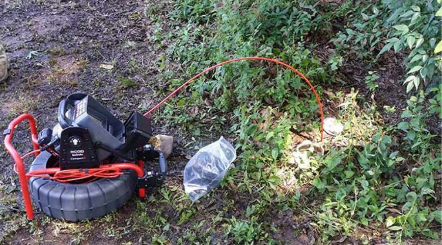Sewer inspection camera system by The Bosworth Company, featuring a reel, monitor, and illuminated cable on grass.
