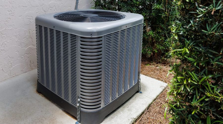 Air conditioning unit on a concrete slab, surrounded by bushes, showcasing The Bosworth Company's HVAC solutions.